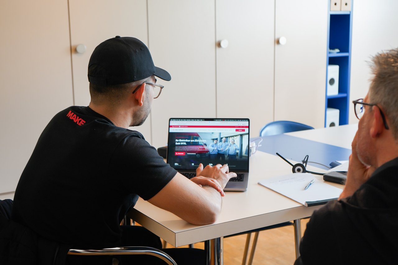 Zwei Männer betrachten einen Laptop auf einem Schreibtisch in einem Büro.